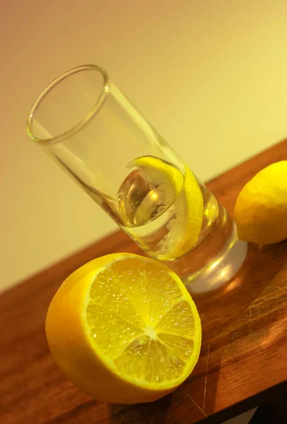 Vodka o gin in un bicchiere bicchierino con una fetta di limone e un limone tagliato a metà su un tagliere di legno. Sfondo rosso — Foto Stock