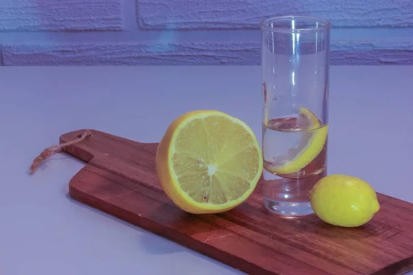 Wodka oder Gin in einem Schnapsglas mit einer Zitronenscheibe darin und einer halbierten Zitrone auf einem Holzschneidebrett. Lila Hintergrund — Stockfoto