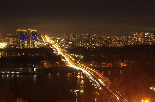 Blick auf die Stadt bei Nacht bei kaltem Wetter, Licht in den Fenstern von Hochhäusern und verschwommene Scheinwerfer von Autos auf der Autobahn. Kiew, Ukraine, europäische Stadt — Stockfoto