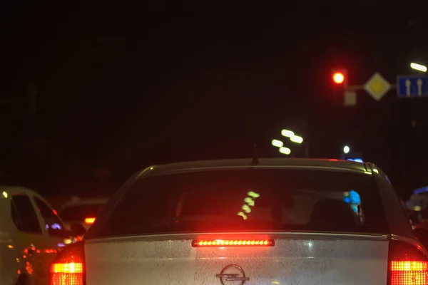 Серый грязный автомобиль Opel, стоящий в пробке на красный светофор ночью, знаки, указывающие дорогу впереди — стоковое фото