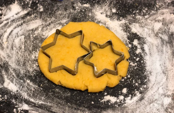 Moldes de corte de galletas en forma de estrella y masa amarilla recién amasada en el interior, tabla de cortar negro espolvoreada con harina blanca. Pasteles saludables caseros — Foto de Stock