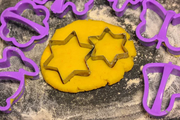 Star-shaped cookie cutter molds and freshly kneaded yellow dough inside, black cutting board sprinkled with white flour. Homemade wholesome pastries