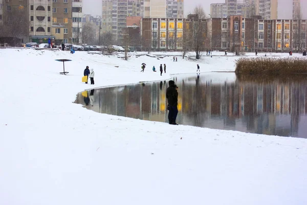 Eine wunderschöne Winterlandschaft, Menschen, die am Nachmittag zwischen den Hochhäusern am See spazieren gehen, das Leben in einer Großstadt — Stockfoto