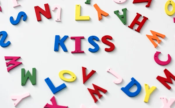 Kiss - a word of multicolored letters on a white table background, English or American Flat Lay alphabet. Valentines Day. — Stock Photo, Image