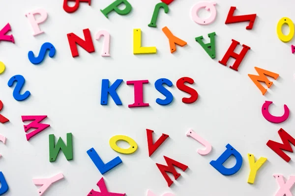 Kiss - a word of multicolored letters on a white table background, English or American Flat Lay alphabet. Valentines Day. — Stock Photo, Image