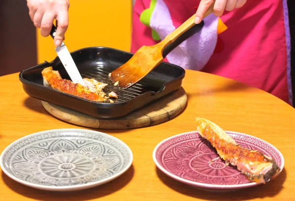 Il pesce rosso ha fritto su una padella per friggere nera, cucini in un grembiule che mette il cibo sano su piatti, i frutti di mare mediterranei — Foto Stock