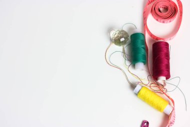 Çok renkli iplik makaraları, pembe mezura ve beyaz bir masa üzerinde pembe bir iğne. Örgü işi, dikiş ve giysilerin tamiri. Mesaj için yer var. Yüksek kalite fotoğraf
