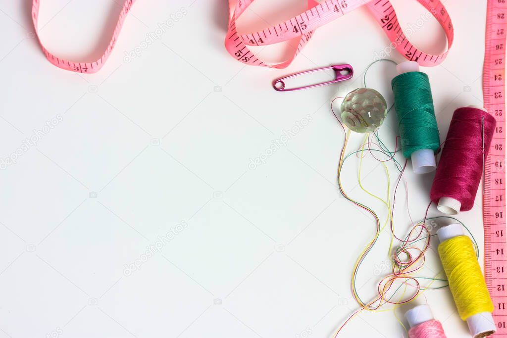 Reels of multicolored thread, pink measuring tape, and a pink pin on a white table flatlay. Needlework, sewing, and repair of the clothes. Space for text. High quality photo
