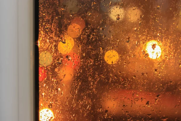 ガラスの窓枠と雨 夜の雨 市内の窓の外には車のヘッドライトと街灯が点灯している 春や秋の悪天候 オレンジの背景 高品質の写真 — ストック写真