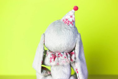 Açık yeşil arka planda oyuncak bir tavşanın arka görüntüsü. Mutlu Paskalyalar. Paskalya için kartpostal. Kırmızı ponponu olan komik şapkalı şirin bir Paskalya tavşanı..