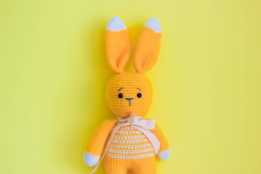 Sarı arka planda şirin bir Paskalya tavşanı oyuncağı. Paskalya minimalizmin kutlu olsun. Paskalya için kartpostal. Tebrik mesajı için uygun bir yer. Uzun kulaklı üzgün bir oyuncak tavşan. El yapımı oyuncaklar..