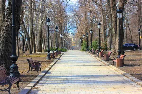 A cobblestone path, going away, wooden benches, black lanterns in a city park. — Stock Photo, Image