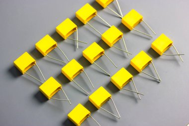 Sarı film kondansatörleri gri arkaplan görüntüsünde izole edildi. Gri yüzeyde kontrastlı gölgelerle birlikte birçok kare şeklindeki plastik elektronik radyo bileşenleri. Seçici odak.