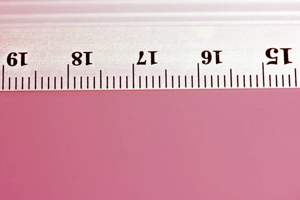Metal ruler close-up on pink background. Top view of a simple ruler with centimeters, millimeters, units of length measurement indicators. Equipment for study. Tools for schoolchildren, students.