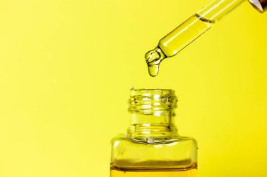 Sıcak sarı arka planda, damlatıcının ucunda bir damla bronzlaştırıcı yağ. Sıcak yaz günlerinde yüz ve vücudun derisini korumak için güneş yağı ile şeffaf cam şişe. Yüz Bakımı Serumu. 