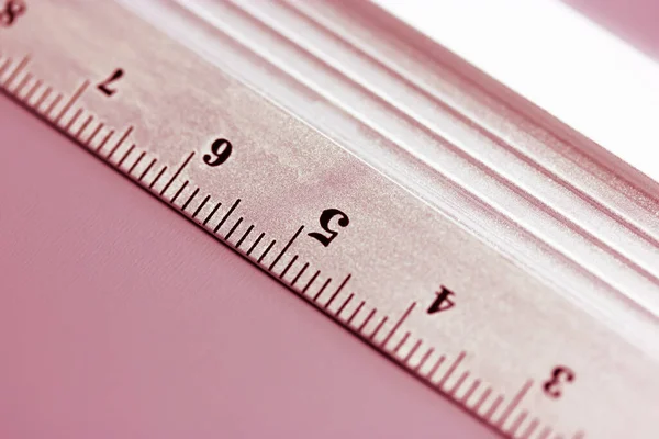 Metal ruler close-up on pink background. Top view of a simple ruler with centimeters, millimeters, units of length measurement indicators. Equipment for study. Tools for schoolchildren, students.