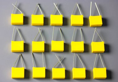 Sarı film kondansatörleri gri arkaplan görüntüsünde izole edildi. Gri yüzeyde kontrastlı gölgelerle birlikte birçok kare şeklindeki plastik elektronik radyo bileşenleri. Seçici odak.