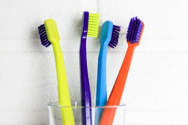 Plastik renkli diş fırçaları seti - yeşil, mavi, kırmızı, mor - beyaz arka plandaki şeffaf camlarda. Dört parlak renkli, yumuşak diş fırçasıyla tuğla duvara yaslanmış bir kupa. Diş bakımı. 