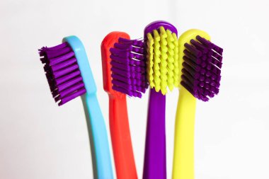 Plastik renkli diş fırçaları seti - yeşil, mavi, kırmızı, mor - beyaz arka plandaki şeffaf camlarda. Dört parlak renkli, yumuşak diş fırçasıyla tuğla duvara yaslanmış bir kupa. Diş bakımı. 