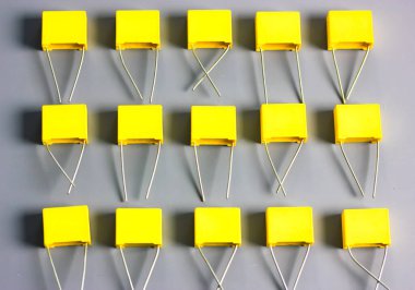 Sarı film kondansatörleri gri arkaplan görüntüsünde izole edildi. Gri yüzeyde kontrastlı gölgelerle birlikte birçok kare şeklindeki plastik elektronik radyo bileşenleri. Seçici odak.