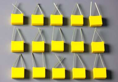 Sarı film kondansatörleri gri arkaplan görüntüsünde izole edildi. Gri yüzeyde kontrastlı gölgelerle birlikte birçok kare şeklindeki plastik elektronik radyo bileşenleri. Seçici odak.