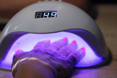 Kadın eli UV LED lambanın içinde jel metoduyla pembe tırnakları kurutmak için, plaka kaplaması için. Manikür işlemi. Güzellik salonunda yeni uygulanan jel ojeleri ya da hibrit ojeler, güzellik uzmanı. 