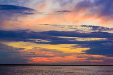 Deniz kıyısında güzel bir gün batımı. Çok renkli mavi-menekşe-turuncu-sarı gökyüzü ve gün batımında görkemli bulutlar. Sessiz su. Ufukta dalgalar var. Seyahat tatili, dinlenme zamanı konsepti.