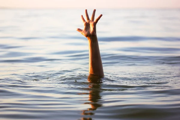 A man is drowning in water. A hand peeks out from under a water. A drowning person needs help, rescue. A risk, danger for living in the sea, river, ocean, pond. Death, SOS concept. Drowning victim