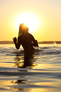 Suda oynayan mutlu çocukların silueti. Çocuklar eğlenir, eğlenir, deniz, göl, gün batımında nehir gibi sakin bir suya atlarlar. Yaz tatilleri, sahilde tatiller. Mutlu bir çocukluk. Su sıçrat.. 