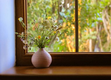 Bouquet of different wildflowers in a pink vase on a wooden window sill against a window at summer sunny day. Flowers in the home interior. Cosy homy atmosphere. Place for text. Natural background. clipart