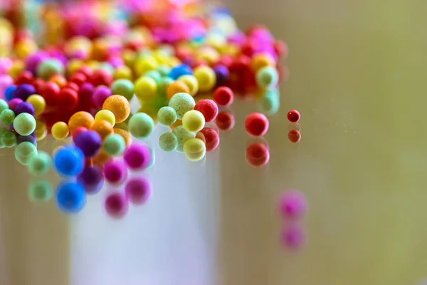 Foam polystyrene round bright colorful beads are reflected on a surface of a glass, mirror. Multicolored pearls floating down, hanging in the air. Foam spherical background. Celebration, fun concept.