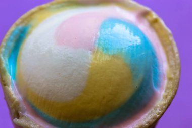 Yukarıdan mor arkaplan manzaralı waffle bardağındaki çok renkli dondurma. 2021 yazının modaya uygun renkleri. Pastel mavi, pembe, sarı. Yüksek kalorili tatlı atıştırmalık. Yaz yemekleri konsepti.