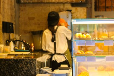 Arkadan bakan bayan barista müşteriye portakal suyu hazırlar. Tanınmayan bir kafe çalışanı, bistro çalışanı. Seçici odaklanma. Bulanık fotoğrafçılık. Önplanda hamur işleriyle karşılık ver.