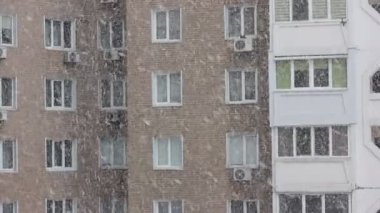 Soğuk kış mevsiminde apartman penceresinden, kapalı mekan manzarası. Büyük kar taneleri gündüzleri yavaşça dışarı düşüyor. Yüksek katlı tuğlalı bir evin birçok penceresi. Şehirde kar fırtınası. Şehir hayatı