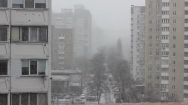 Düz balkondan çok katlı panellere, binalara, evlere, pencerelere ve soğuk bir kış gününde soğuk bir caddeye bakan sokağa bakın. Kar yağışı, kar taneleri yavaşça düşüyor.