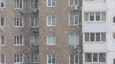 Apartman penceresinden bir ev manzarası. Soğuk kış mevsiminde gündüz vakti açık havada kar taneleri düşüyor. Çok katlı bir tuğla binanın birçok penceresi. Şehirde kar fırtınası. Şehir hayatı