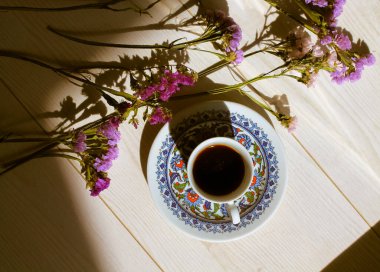 Geleneksel mavi porselen fincanda, beyaz ahşap zemin manzaralı çay tabağında Türk kahvesi. Karşıt gölgeler. Sabah ışığında sıcak espresso içilir. Kurumuş mor çiçeklerin bileşimi.. 
