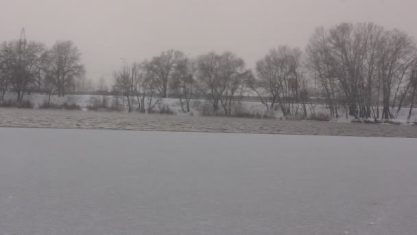 A neve cai sobre um lago calmo, River. Má visibilidade. Uma bela paisagem natural nevada. A primeira neve branca lentamente cai de um céu a um chão. Árvores nuas num horizonte. Dezembro, Janeiro, Fevereiro. — Vídeo de Stock