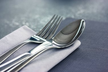 Çorba kaşığı ve metal çatal gri yüzey manzaralı gri bir peçetenin üzerinde yatar. Masa düzenleme, restoranda kumaş, kafe, ev mutfağı. Gri tekstil havlusu. Yukarıdaki çatal bıçak görüntüsünü kapat.