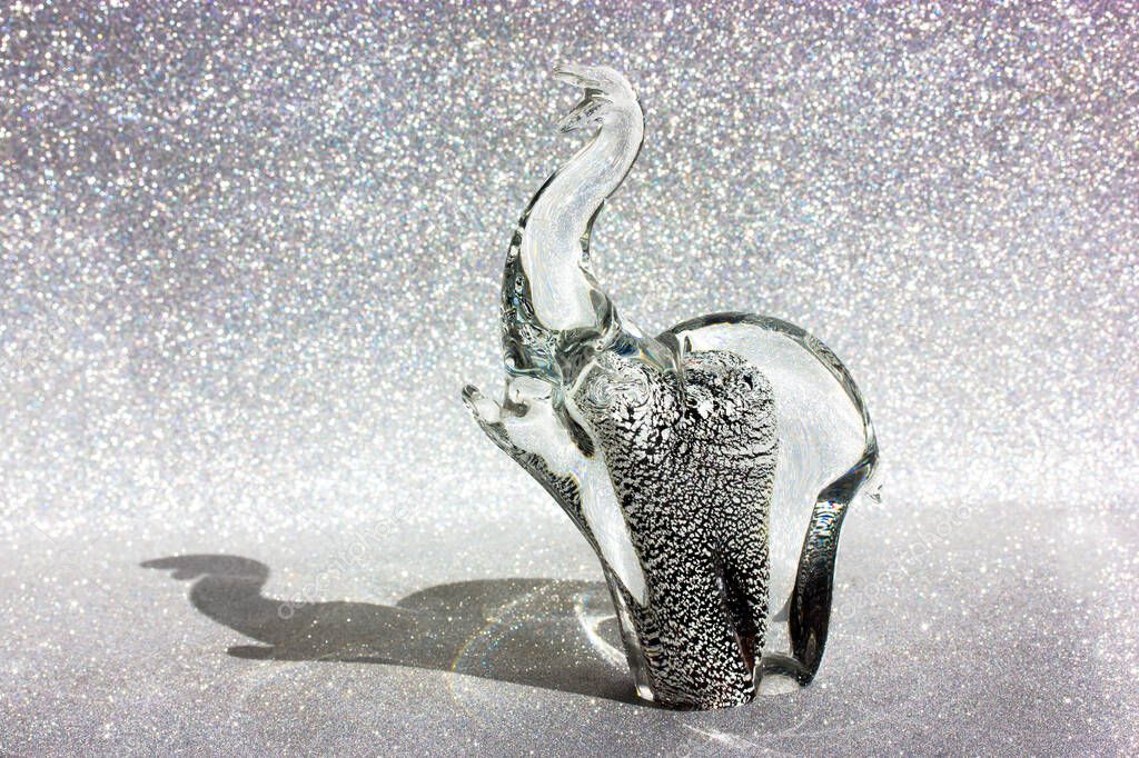 Elephant figure made of Murano glass, contrasting shadow on a silver shining background. Animal figurine. Talisman protects against evil spirits. Souvenir from India, Thailand or Italy. Modern decor.