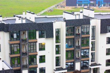 Yeni, beyaz, çok katlı apartmanın çatısı siyah. Pencereden bir manzara. Çağdaş mimari. Pencereleri camlı, bir apartman bloğundaki balkonlar. Mahalle sakinleri. Arkadaki yeşil çimenler