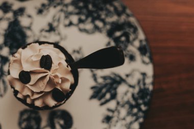 Delicious coffee dessert with chocolate spoon on a floral patterned plate. This overhead shot captures a delightful dessert featuring coffee beans and a chocolate spoon. 