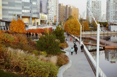 Kyiv, Ukrayna 25 Ekim 2025 Sonbahar şehri rıhtım manzaralı ve renkli ağaçları var. İnsanlar, sakin bir su kütlesinin yanında, sonbahar mevsiminin güzelliğinin tadını çıkararak manzaralı bir yürüyüş yolunda yürürler..