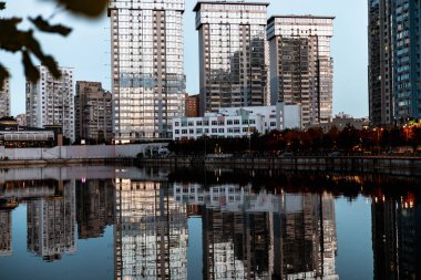 KYIV, Ukrayna 25 Ekim 2025 Modern şehir gökdelenleri alacakaranlıkta suya yansıyan gökdelenler. Yüksek bina yansımaları alacakaranlık gökyüzüne karşı çarpıcı bir görsel ekran oluşturur..