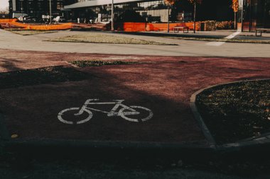 Sıcak öğleden sonra ışığında kırmızı asfalt üzerinde bisiklet yolu işareti olan minimum şehir manzarası. Çevre taşımacılığını, sürdürülebilir yaşam tarzını ve kasvetli tonlarda yaşayan aktif kentsel yaşamı temsil eden modern şehir detayları.