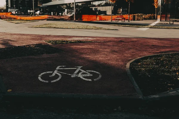 Sıcak öğleden sonra ışığında kırmızı asfalt üzerinde bisiklet yolu işareti olan minimum şehir manzarası. Çevre taşımacılığını, sürdürülebilir yaşam tarzını ve kasvetli tonlarda yaşayan aktif kentsel yaşamı temsil eden modern şehir detayları.