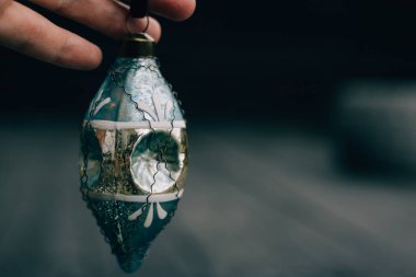 Karanlık bir arka planda el ele tutuştuğumuz klasik bir Noel süsü. Bu antika Noel dekorasyonu bayram nostaljisi ve şenlik dekorunun güzel bir örneğidir. Mavi cam Noel ağacı süsü