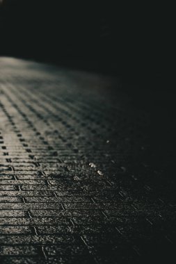 Yağmurdan sonra ıslak tuğla yolu olan karanlık bir sokak. Karanlığa giden boş tuğlalı yolun karamsar, atmosferik bir görüntüsü. Arka planda bir bina var. Şehir caddesinin soyut dramatik görüntüsü.