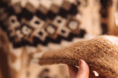 Yumuşak, desenli kahverengi ve bej bir kazağı tutan bir elin yakın çekimi. Bir insanın eli nazikçe sıcacık, sıcak bir süveterin bir kısmını tutuyor ve karmaşık örgü tasarımını gösteriyor. Mevsimlik sıcak kadın kıyafetleri.