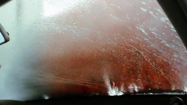 Penceresinde su damlacıkları olan bir araba yıkama yeri. Araba yıkamanın turuncu fırçaları bir arabanın ıslak penceresinden görülür ve eşsiz bir perspektif yaratır. Çevre dostu araba yıkama işlemi. 